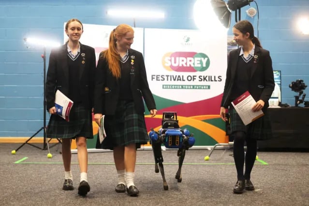 Three school students walk with the Balfour Beatty robodog at the festival